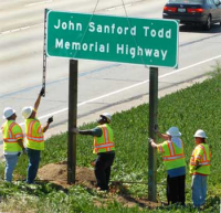 Workers erecting road sign with text John Sanford Todd Memorial Highway