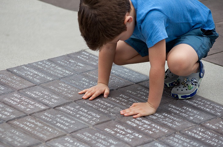 A small child bends over a pavement of memorial bricks