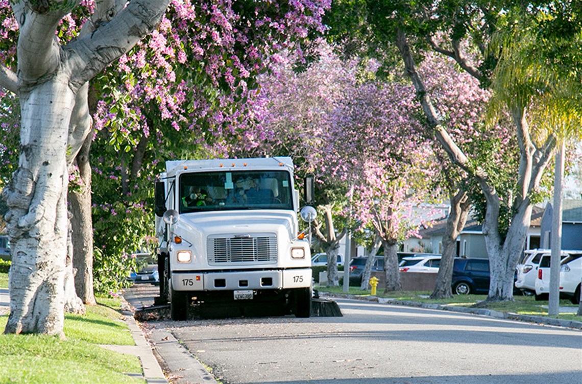 Street Sweeper driving residential street with trees in bloom