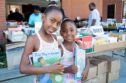 Two smiling girls holding books at book fair